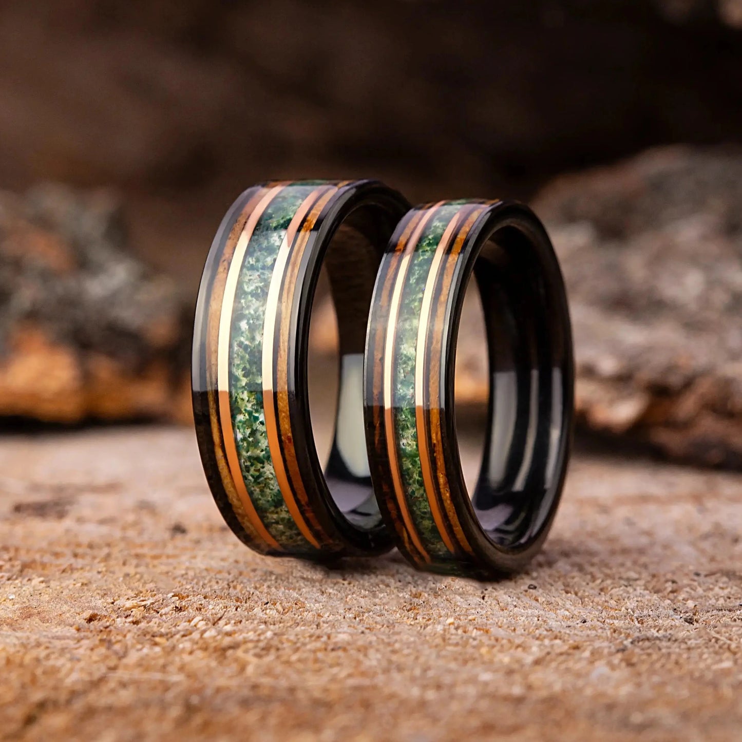 Two rings with green and gold inlay on a wooden surface