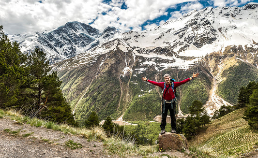 Man is staying on a top of a mountain with hands spread wide open 