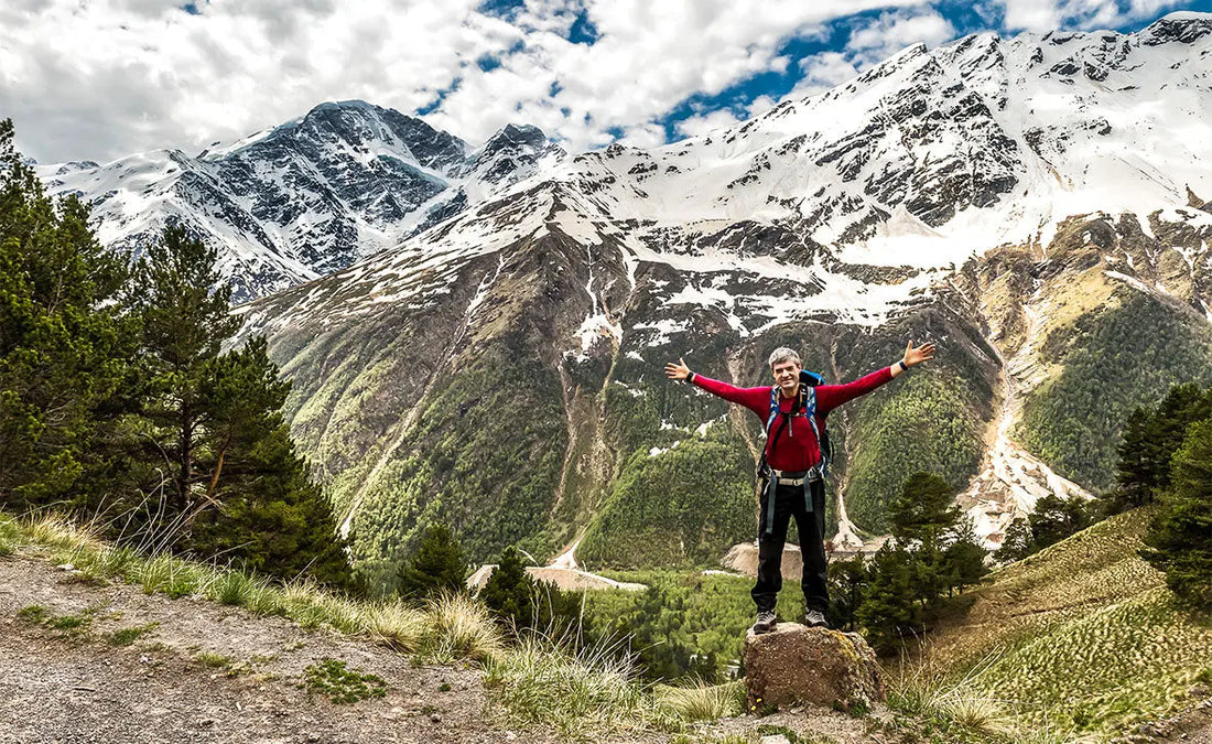 Man is staying on a top of a mountain with hands spread wide open 