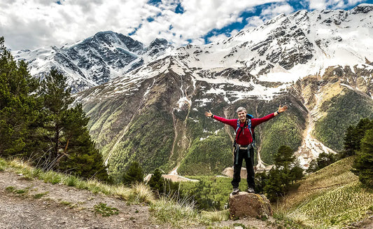 Man is staying on a top of a mountain with hands spread wide open 