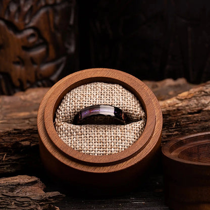 Hammered black tungsten ring with opal and meteorite. The ring is placed inside a round wooden box