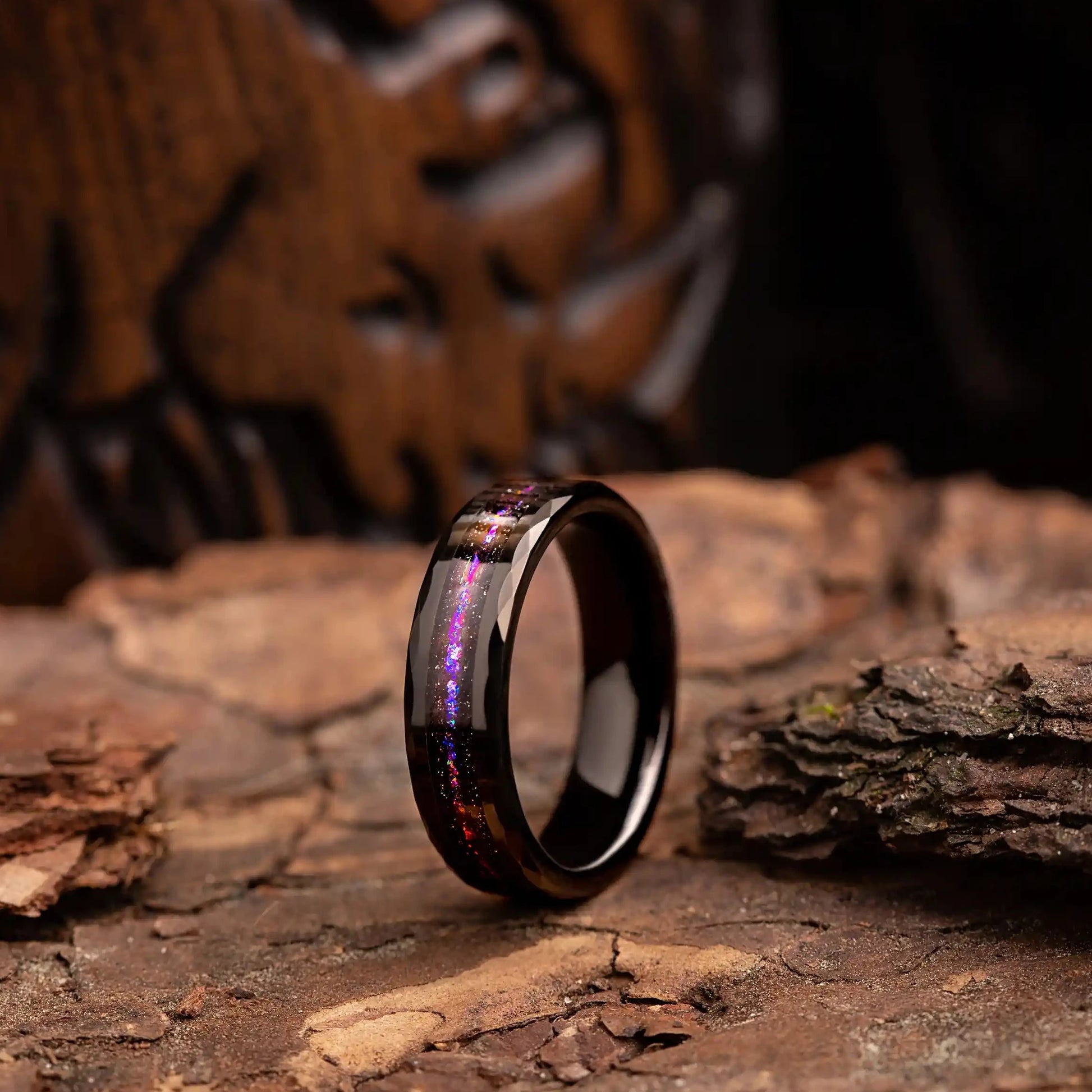 Hammered black tungsten ring with opal and meteorite. The ring is placed on a wood