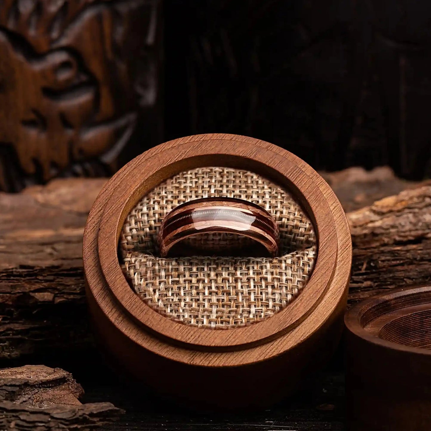 Brown brushed tungsten ring with guitar string and whiskey barrel oak wood. The ring is placed inside a round wooden box.