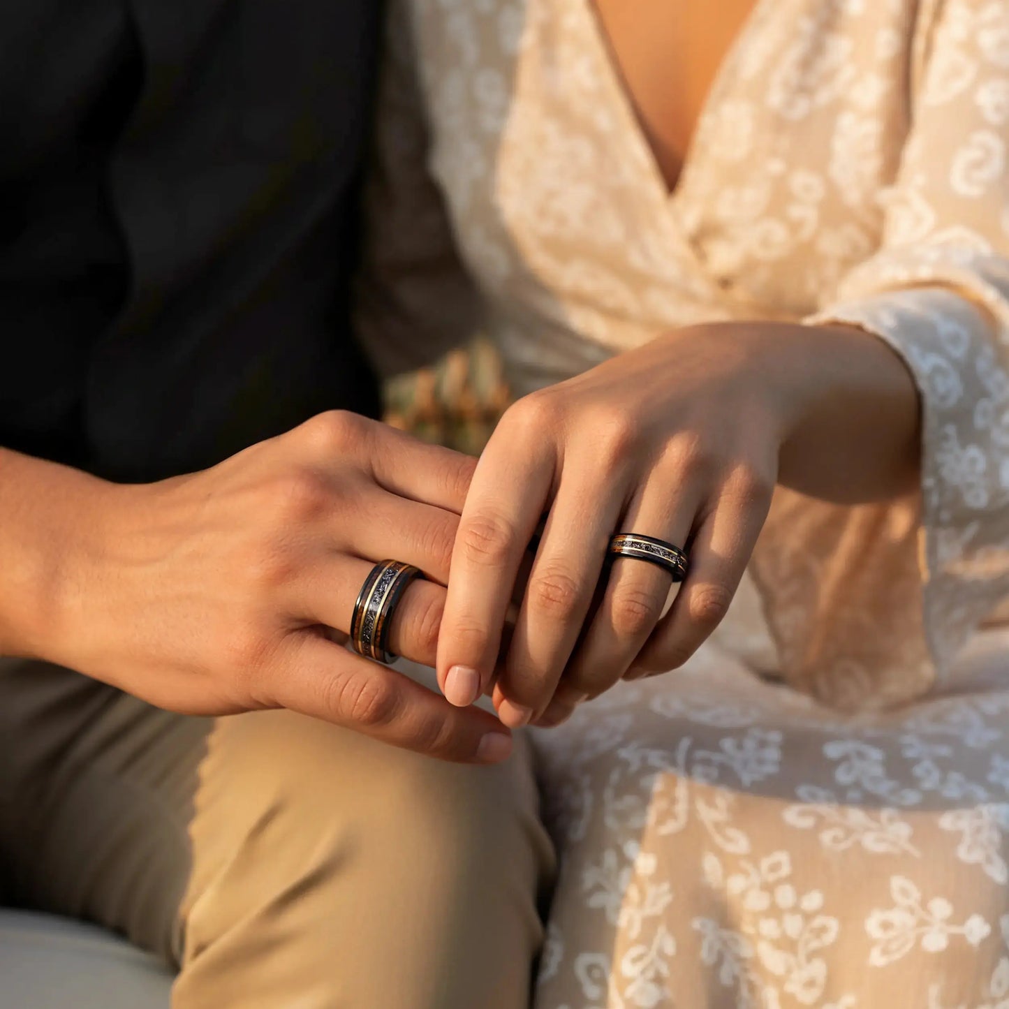 Close-up of two hands with rings, one person wearing a floral dress.