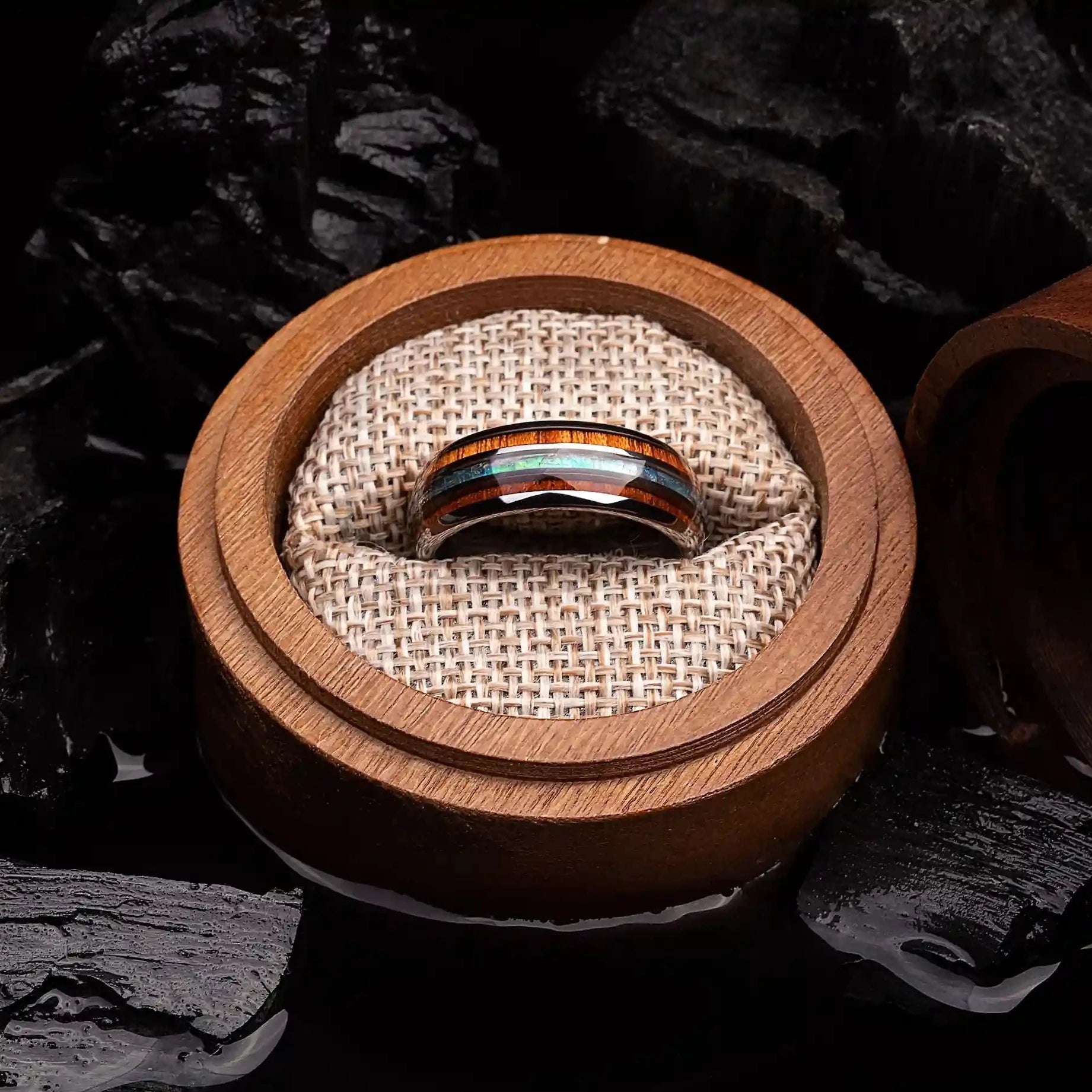 Brushed silver tungsten ring with abalone shell and koa wood. The ring is placed inside a round wooden box.