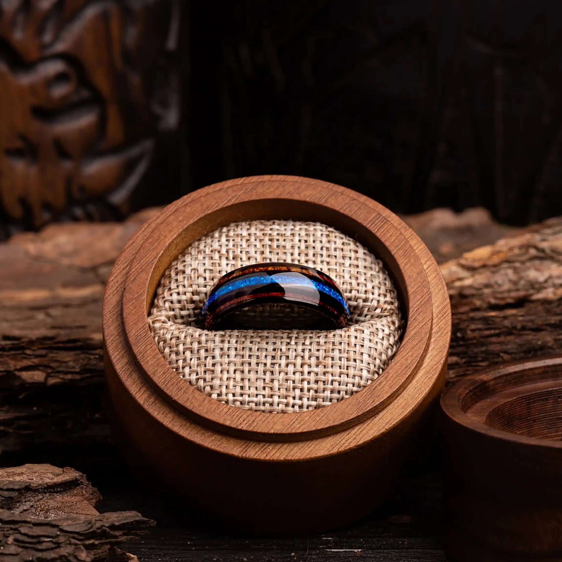 Black polished tungsten ring with blue opal and whiskey barrel oak wood. The ring is placed inside a round wooden box