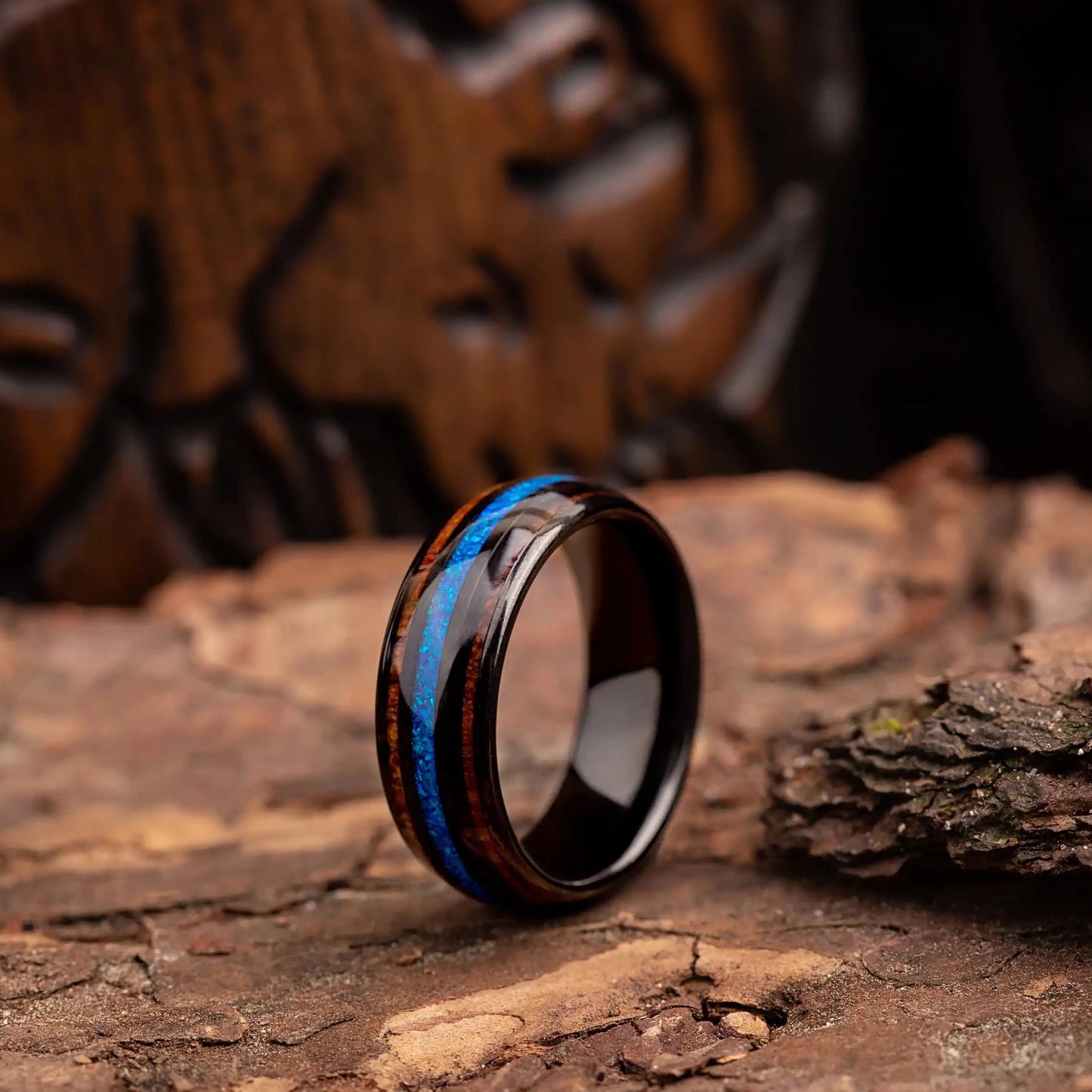 Black polished tungsten ring with blue opal and whiskey barrel. The ring is placed on a wood