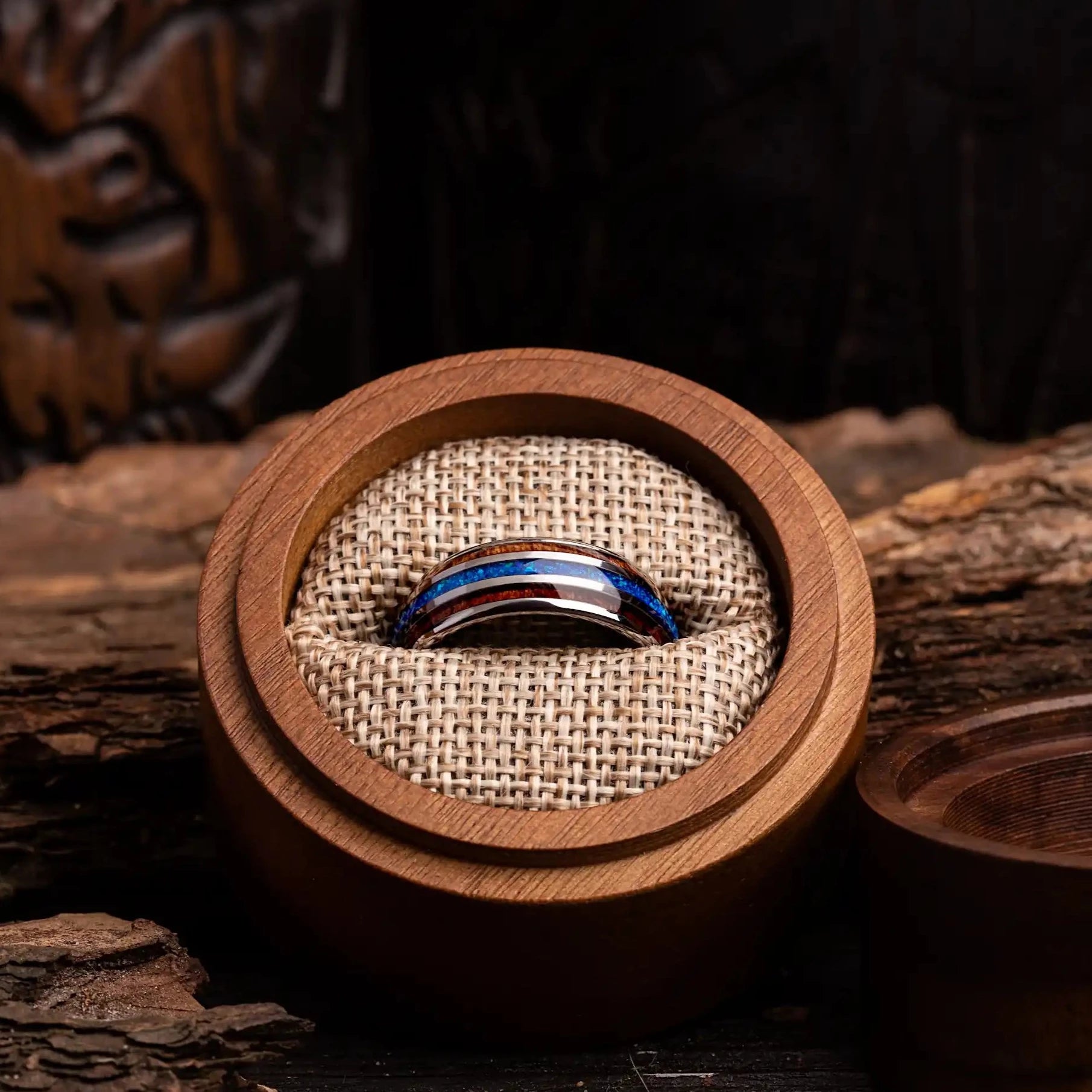 Silver tungsten ring with blue opal and whiskey barrel oak wood. The ring is placed inside a round wooden box