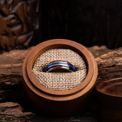 Silver tungsten ring with blue opal and whiskey barrel oak wood. The ring is placed inside a round wooden box