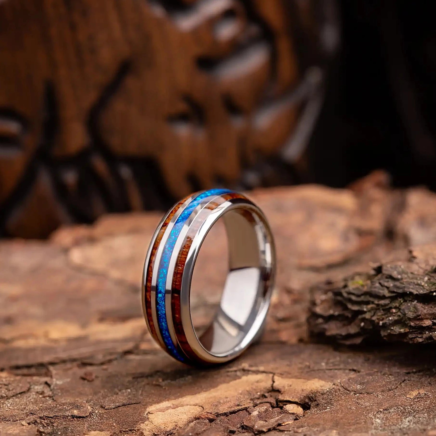 Silver tungsten ring with blue opal and whiskey barrel oak wood. The ring is placed on a wood