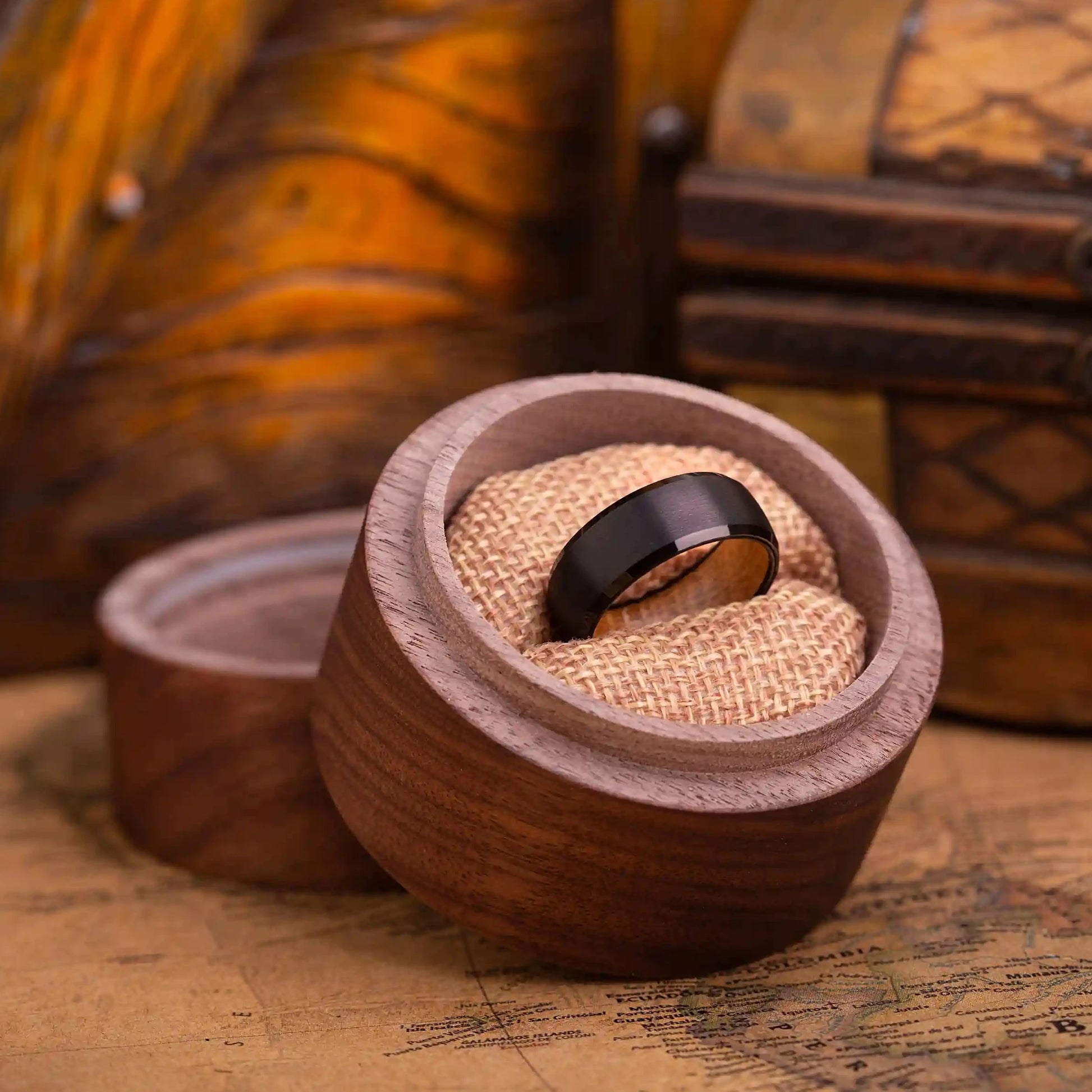 8mm black brushed tungsten ring with whiskey barrel oak wood. The ring is placed inside a round wooden box.