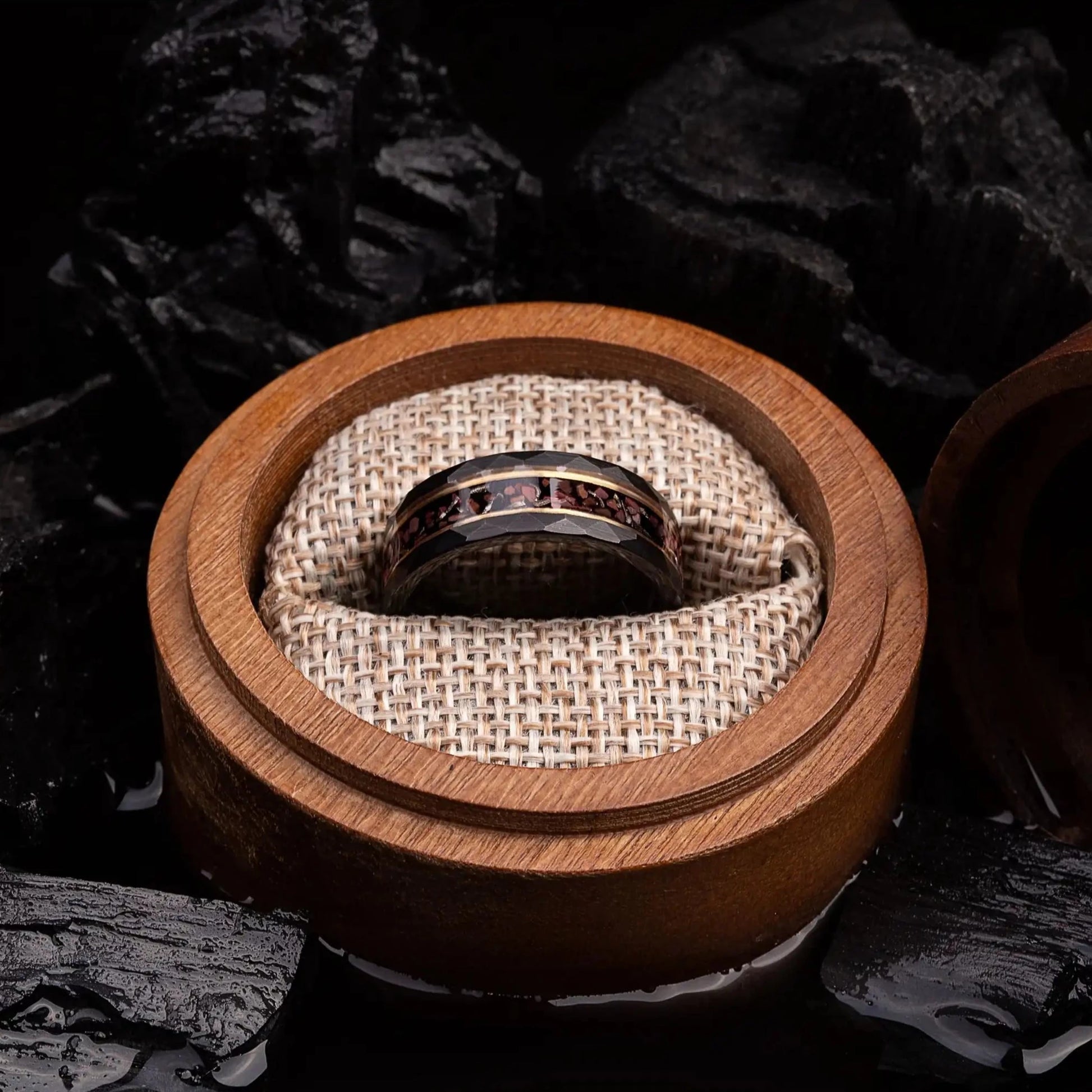 Black hammered tungsten ring with dinosaur bones and meteorite. The ring is placed inside a round wooden box