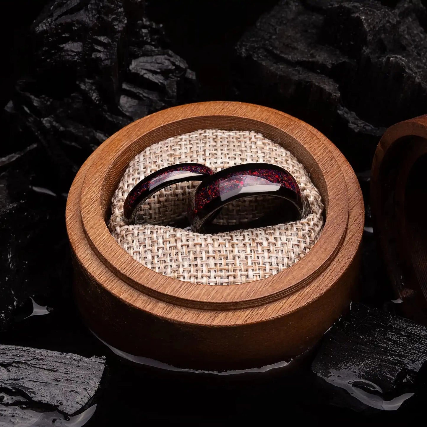 Black tungsten matching ring set with red opal. The ring are placed inside a round wooden box.