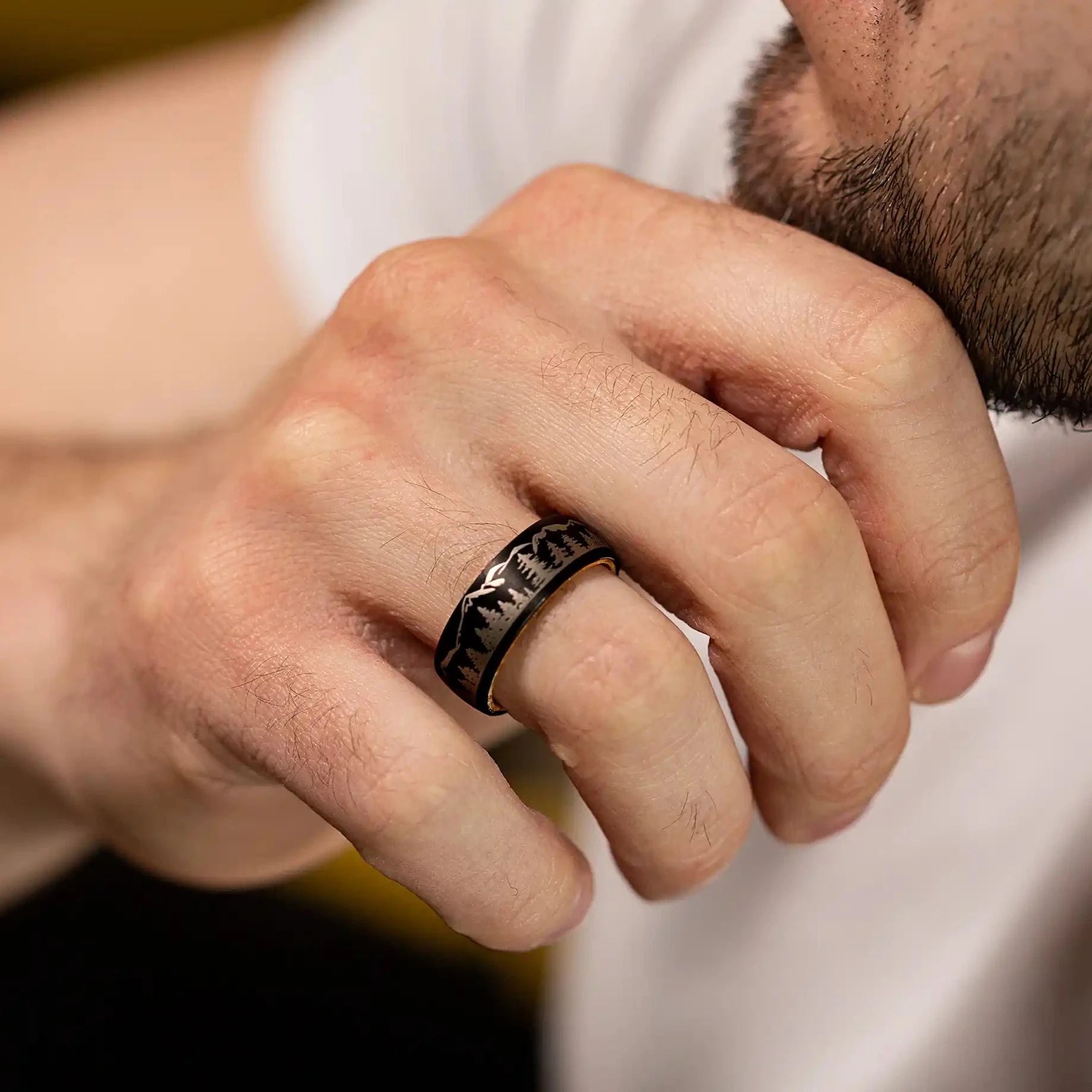 Black tungsten ring with engraved forrest. The ring is on a man's hand