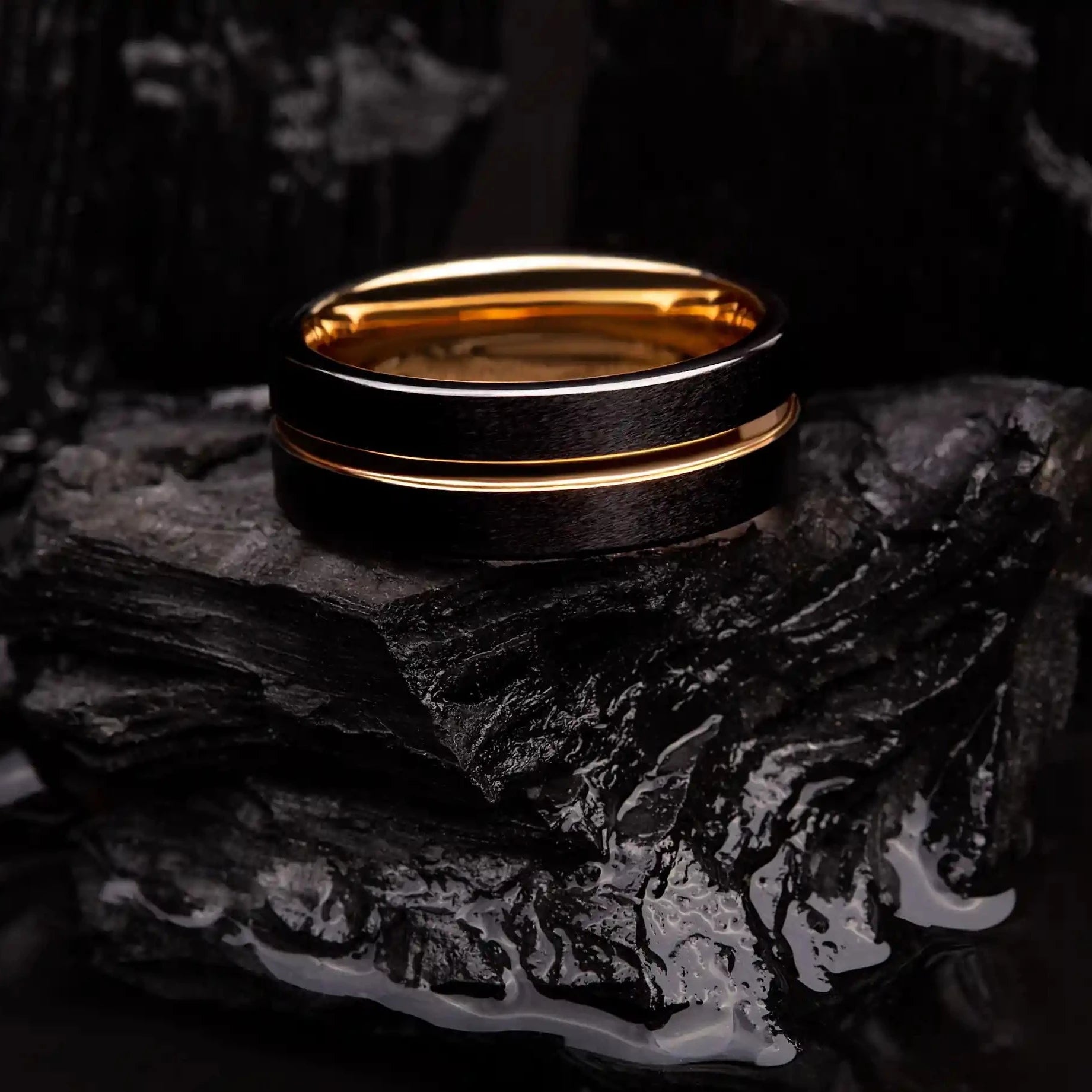 Ring made of black and gold tungsten. The ring is laying on a black coal