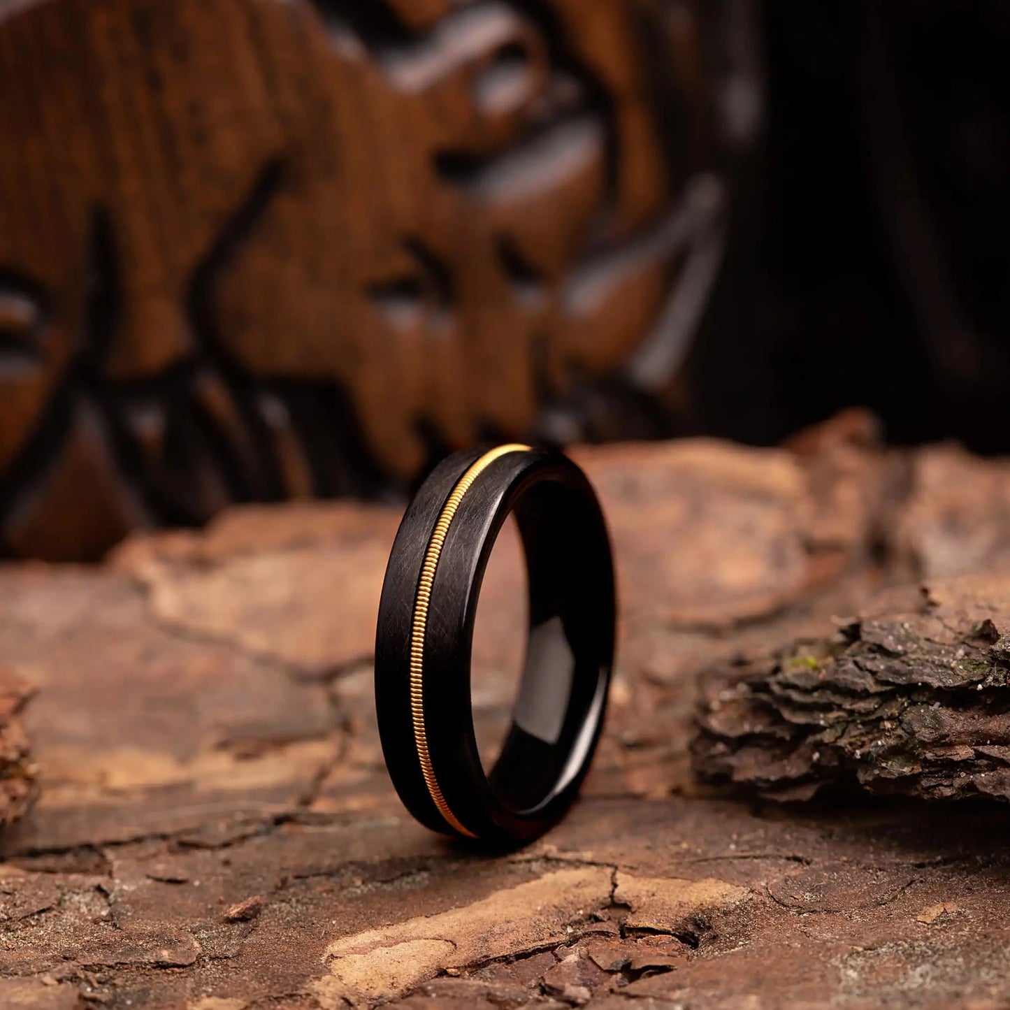 6mm black tungsten ring with guitar string. The ring is placed on a wood