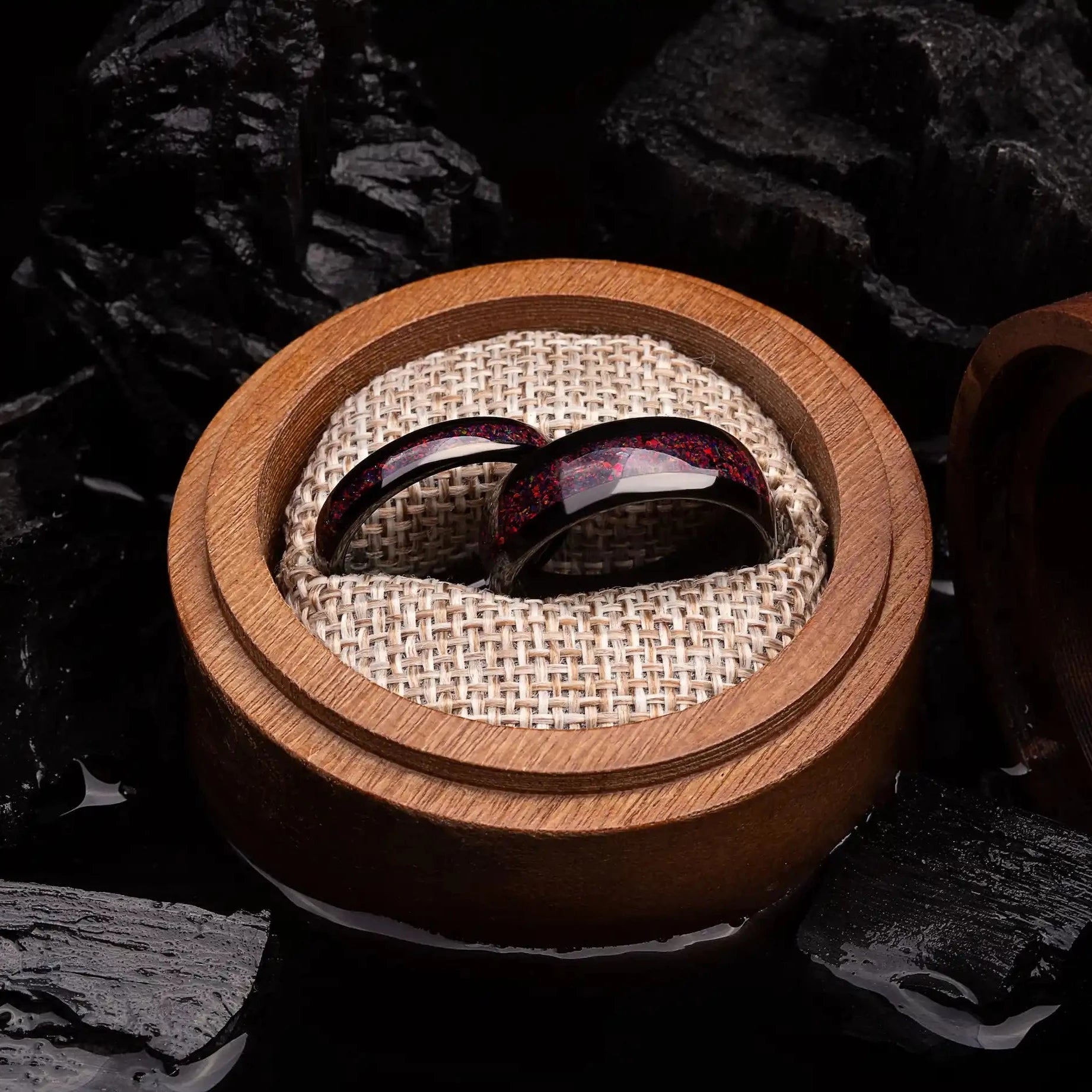 Black tungsten matching ring with red opal. The ring are placed inside a round wooden box.