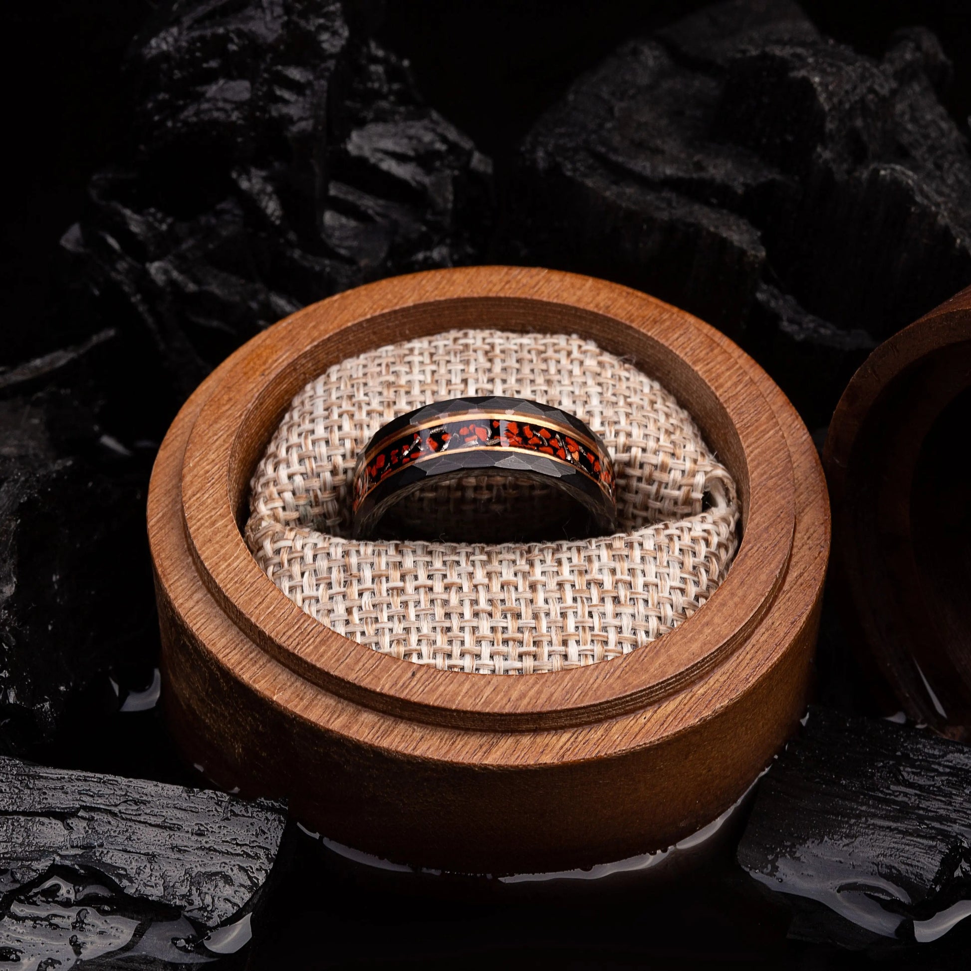 Black hammered tungsten ring with dinosaur bones and meteorite. The ring is placed inside a round wooden box