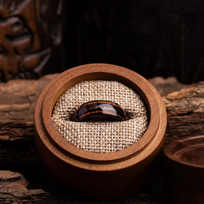 Black tungsten ring with purple opal and whiskey barrel oak wood. The ring is placed inside a round wooden box