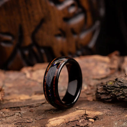 Black tungsten ring with purple opal and whiskey barrel oak wood. The ring is placed on a wood