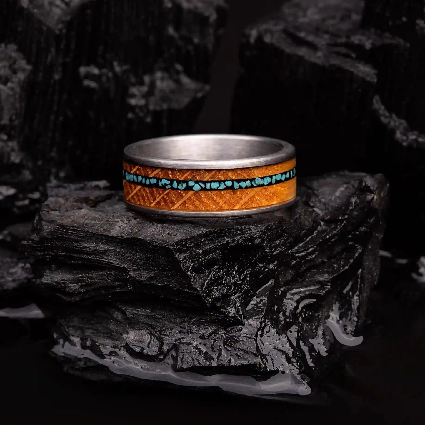 Silver brushed tungsten ring with turquoise and oak wood. The ring is laying on a black coal