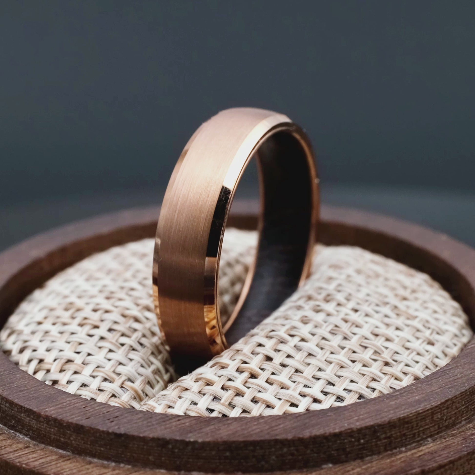 4 mm rose titanium ring with whiskey barrel oak wood inner layer. The ring is placed inside a round wooden box