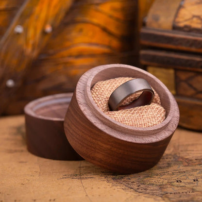 Grey tungsten ring with rosewood inlay. The ring is placed inside a round wooden box.