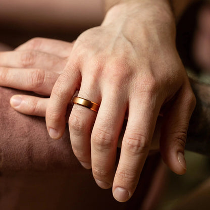 4 mm rose titanium ring with whiskey barrel oak wood inner layer. The ring is on a man's hand