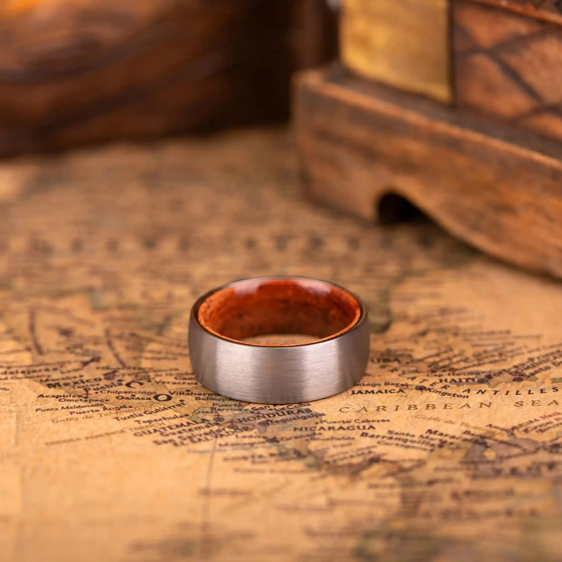 Brushed silver tungsten ring with rosewood inlay. The ring is laying on a map