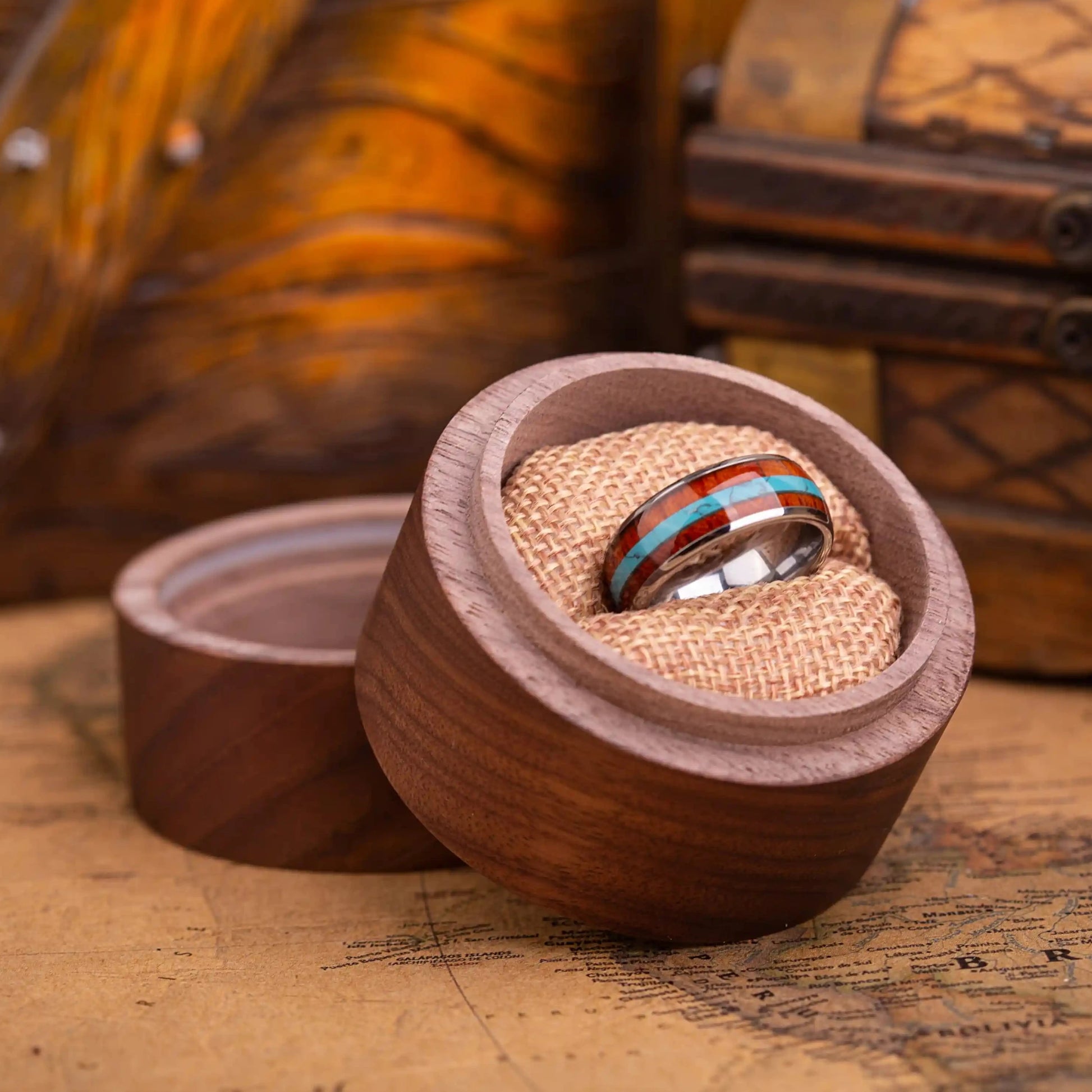 SIlver ring with turquoise and whiskey barrel oak wood in the central inlay. The ring is placed inside a round wooden box