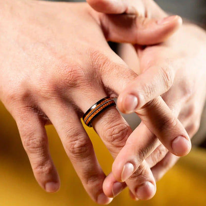 Black brushed tungsten ring with a guitar string and a whiskey barrel oak wood. The ring is on a man's hand