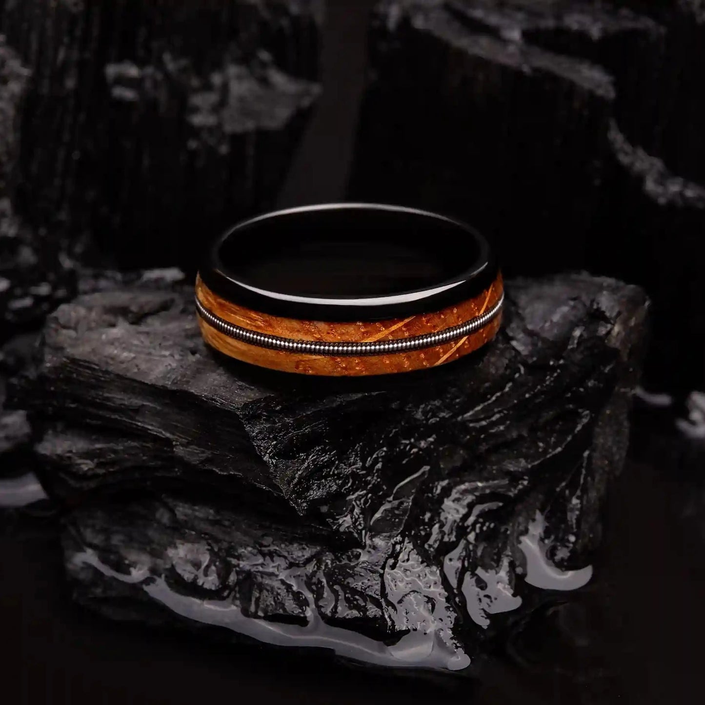 Black brushed tungsten ring with a guitar string and a whiskey barrel oak wood. The ring is laying on a black coal