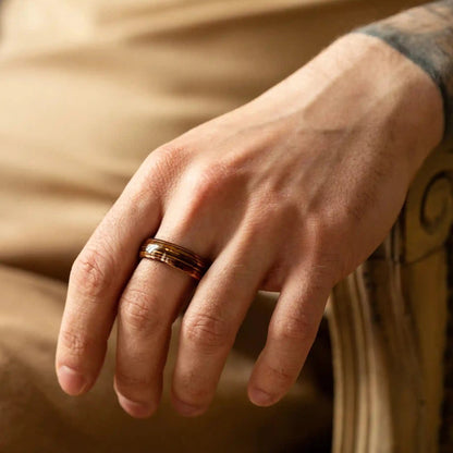 Brown brushed tungsten ring with guitar string and whiskey barrel oak wood. The ring is on a man's hand