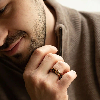 Brown brushed tungsten ring with guitar string and whiskey barrel oak wood. The ring is on a man's hand