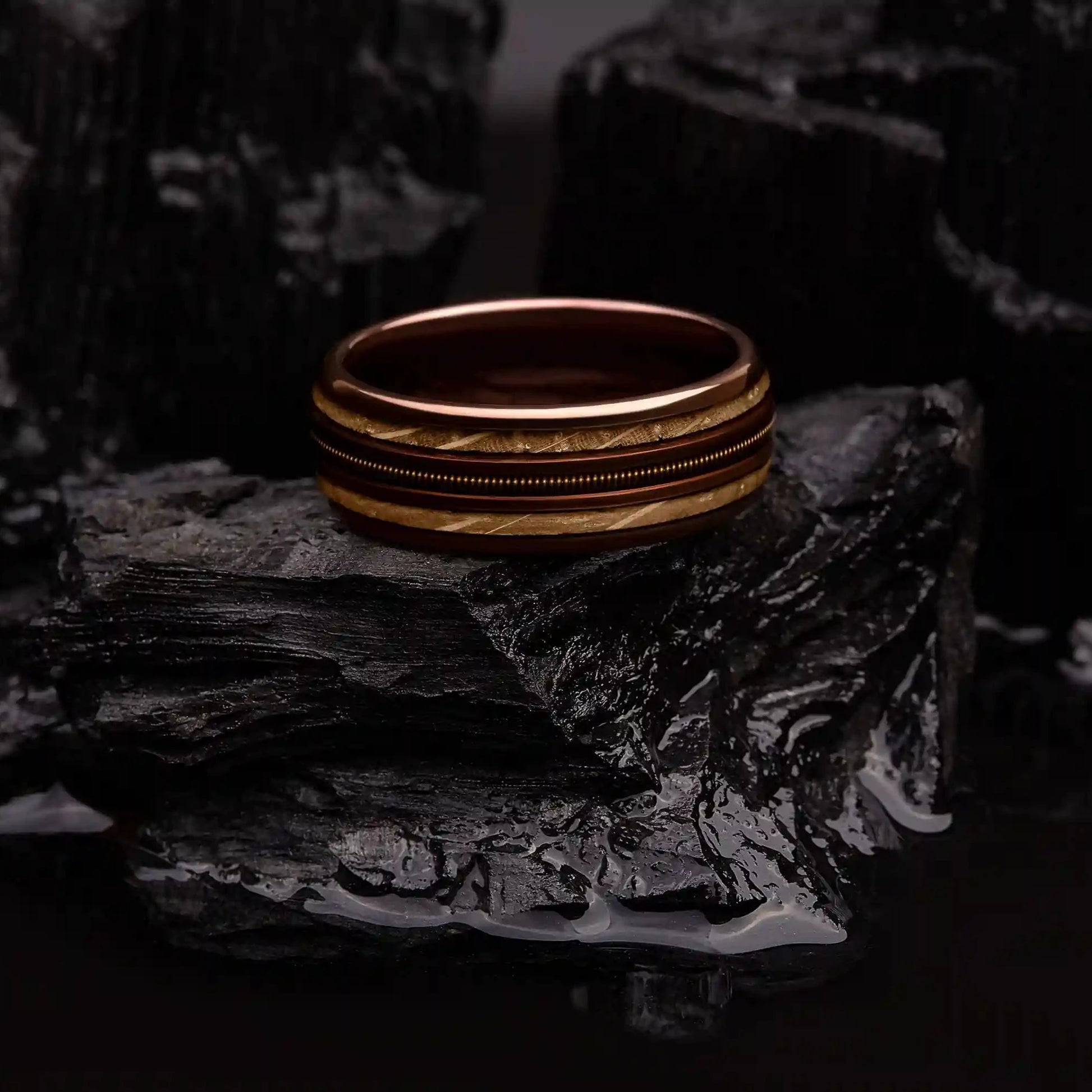 Brown brushed tungsten ring with guitar string and whiskey barrel oak wood. The ring is laying on a black coal