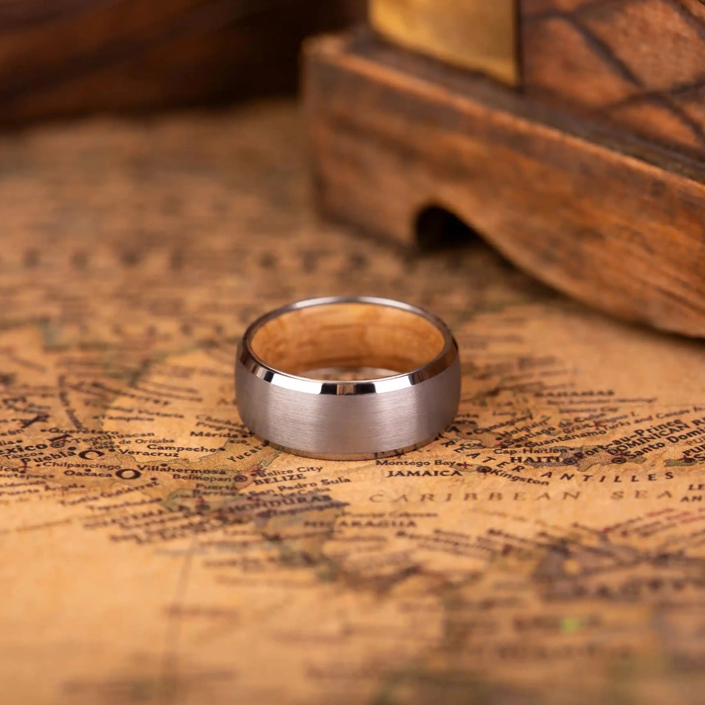 8mm silver brushed tungsten ring with whiskey barrel oak wood inlay. The ring is laying on a map