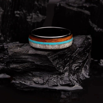 Brushed black tungsten ring with turquoise, koa wood and deer antler. The ring is laying on a black coal