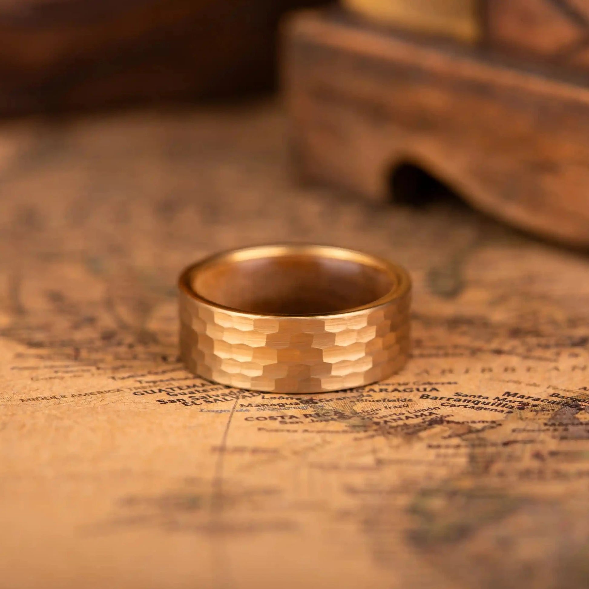 Faceted gold tungsten ring with walnut inlay. The ring is laying on a map