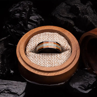 Brushed black tungsten ring with deer antler and whiskey barrel oak wood. The ring is placed inside a round wooden box.