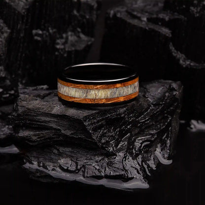 Brushed black tungsten ring with deer antler and whiskey barrel oak wood. The ring is laying on a black coal.